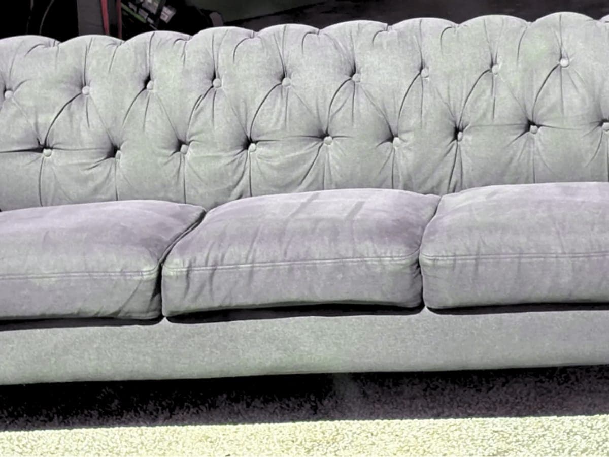 Gray tufted chesterfield sofa after cleaning, cushions full and fabric even instead of replaced