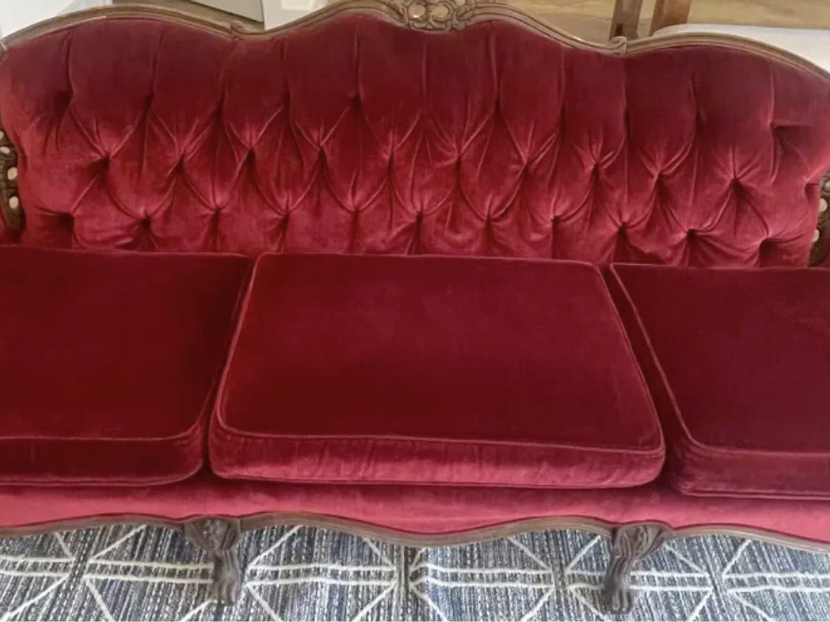 Antique burgundy velvet sofa with a tufted back and carved wood frame after cleaning, the pile groomed in one direction